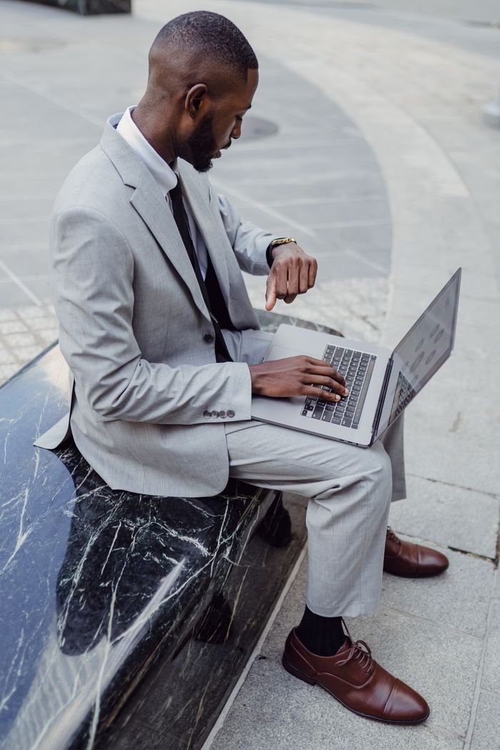 Crafting Captivating Headlines: Your awesome post title goes here A professional man in a suit checks his wristwatch while using a laptop outdoors, portraying modern business.