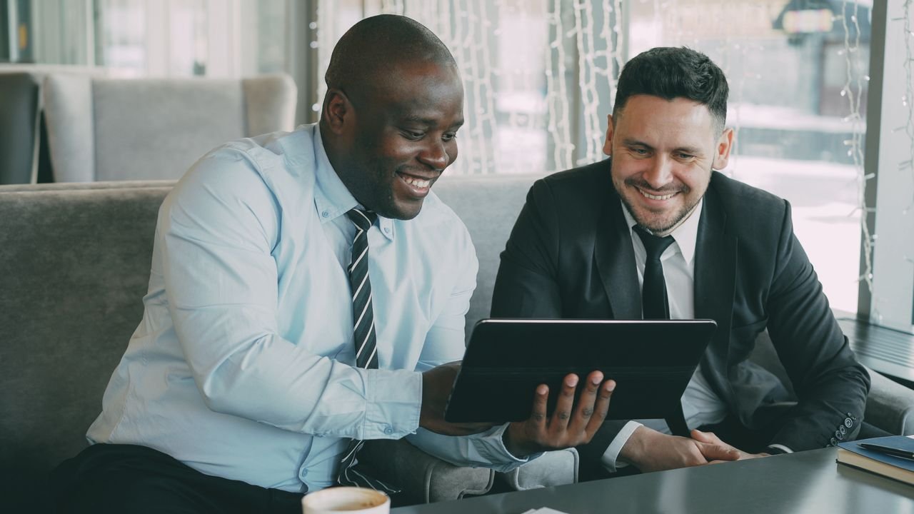 Mastering the First Impression: Your intriguing post title goes here Two businessmen happily collaborating on a digital tablet in a modern cafe setting.