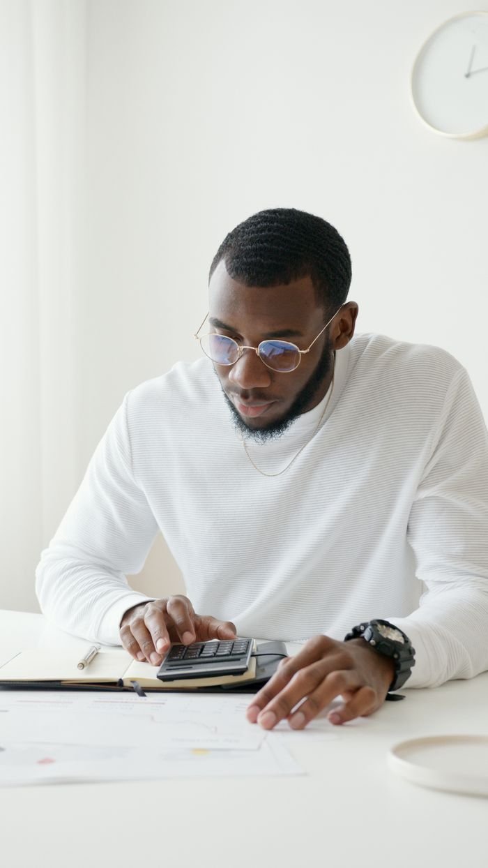 services-03 Man in glasses working on calculations at desk in bright office setting.